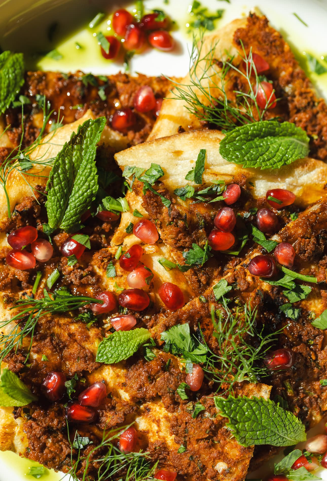 Spiced lamb flatbread scattered with pomegranate seeds, mint, dill and parsley in herb oil