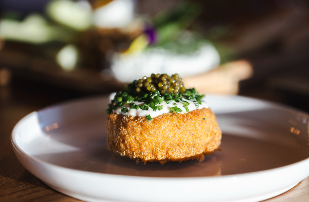 Crisp brioche round topped with crème fraîche, chives and caviar on a white plate