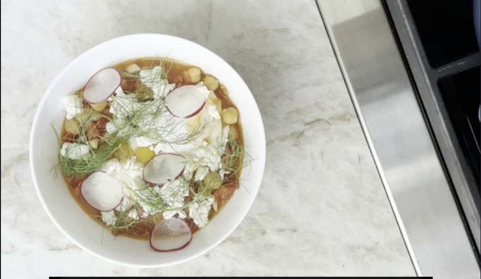 A finished bowl of stewed tomatoes, beans, feta, radish and fennel fronds