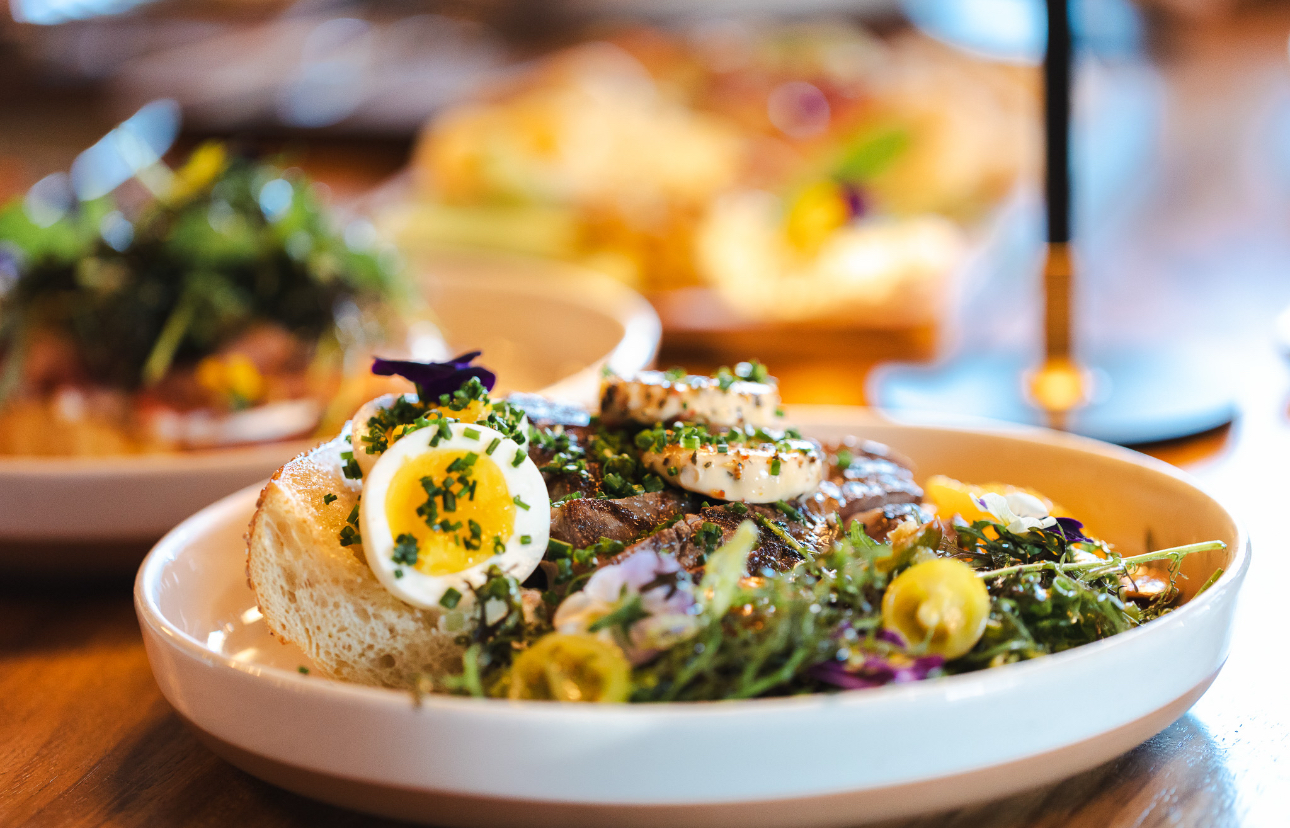 Grilled steak with soft-boiled egg, herb salad and grilled sourdough plated in a wide ceramic bowl