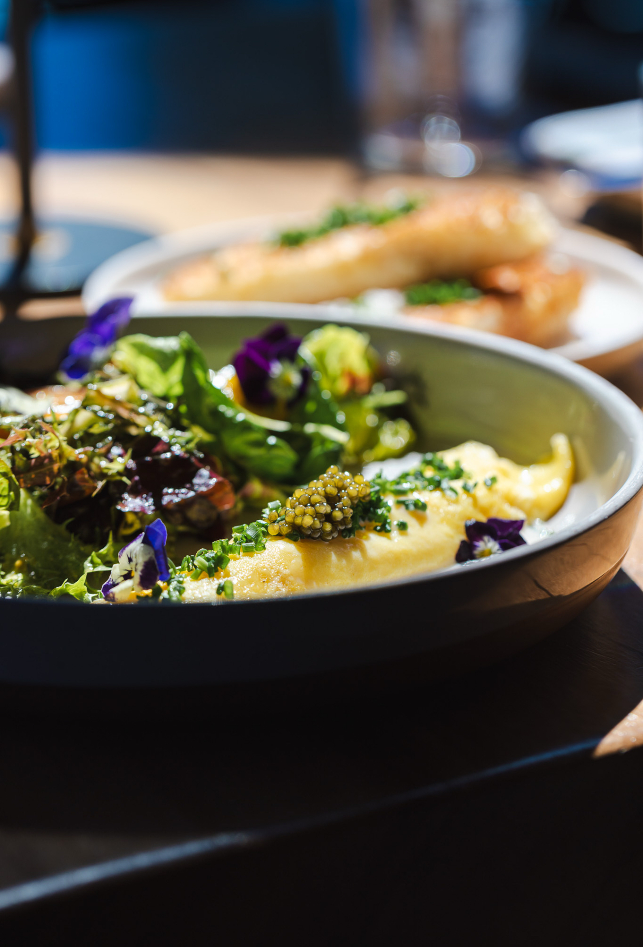 Soft-folded omelette with caviar, chives and a dressed herb salad in a dark ceramic bowl